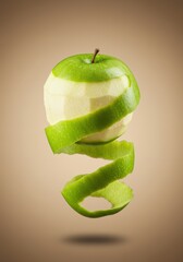 A partially peeled green apple with its peel spiraling downwards, suspended against a warm brown background