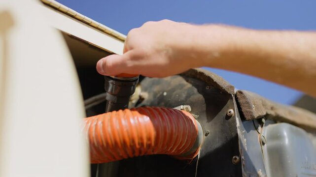 Extreme closeup of man's hand returning oil dipstick into plane engine and screwing cap back on during day time in Kenya