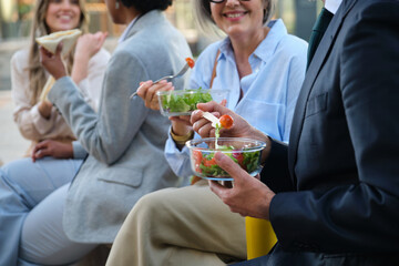 Office workers enjoying a healthy lunch break together outdoors, eating fresh takeaway salads