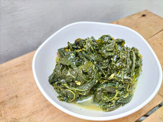 Selective focus. Daun singkong or Cassava leaf curry is a traditional Indonesian dish, made from boiled cassava leaves, seasoning with coconut milk and spicy curry spices. 