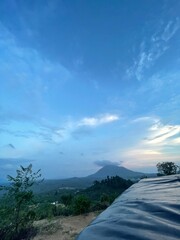 A peaceful morning sky with soft blue hues and gentle clouds above a green forest. Ideal for background use, graphic design, presentations, and travel content.