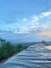 A peaceful morning sky with soft blue hues and gentle clouds above a green forest. Ideal for background use, graphic design, presentations, and travel content.