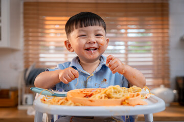 Happy Asian boy with a big smile, messy face, enjoying a fun mealtime.