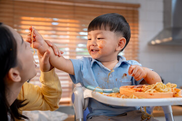 Asian boy feeds spaghetti to mom, a happy family moment.