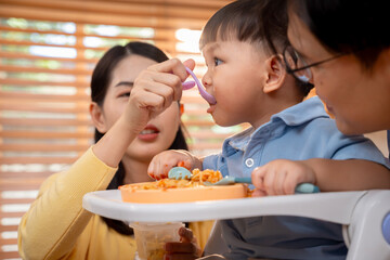 Mom feeds Asian boy, showing love and care during mealtime.