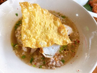 A bowl of spicy and sour tom yum noodle soup with pork, fish balls, peanuts, and herbs. A hearty and flavorful Thai dish.