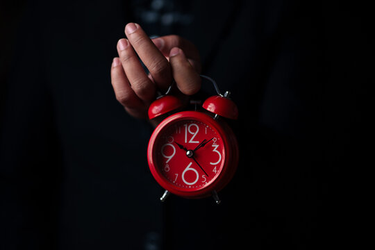 Time management challenge red alarm clock held in hand indoor setting close-up perspective concept of urgency