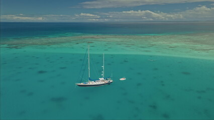 A large sailing vessel with multiple masts is anchored in crystal-clear turquoise waters.