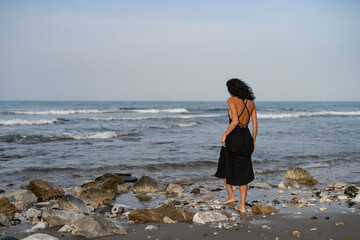 Brunette Woman in Black Dress Standing on Rocks in the Sea
