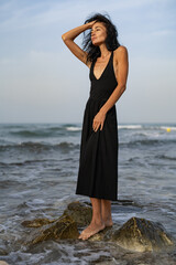 Brunette Woman in Black Dress Standing on Rocks in the Sea