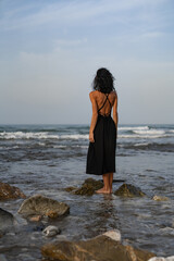 Brunette Woman in Black Dress Standing on Rocks in the Sea