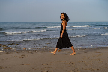 Brunette Woman in Black Dress Walking Along the Beach