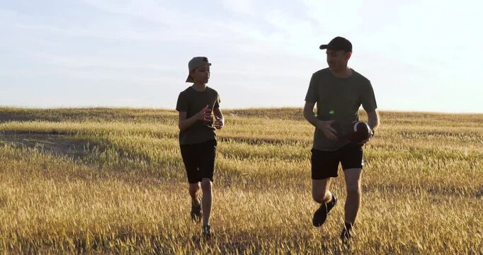 happy child playing american football with dad. joyful child spends holidays playing american football. dad and son run on golden field throwing ball each other. active games of children and parents.