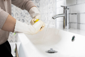 Close-up shot of woman in rubber gloves cleans sink and faucet with a rag and spray in the...
