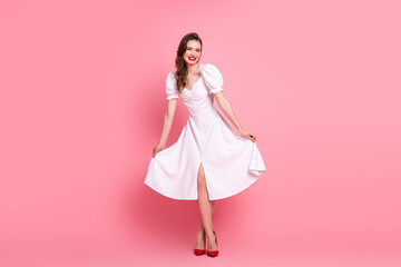 Young stylish woman in white dress smiling on pink background, showcasing cheerful and charming...
