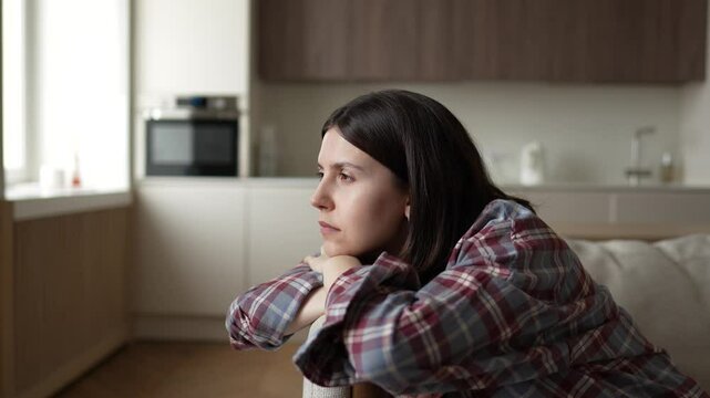 Bored disinterested woman stares blankly out window feeling no motivation, drained of joy with apathy, lack of dopamine. Lost in thoughts sad girl sits at home alone. Low energy mental health concept.