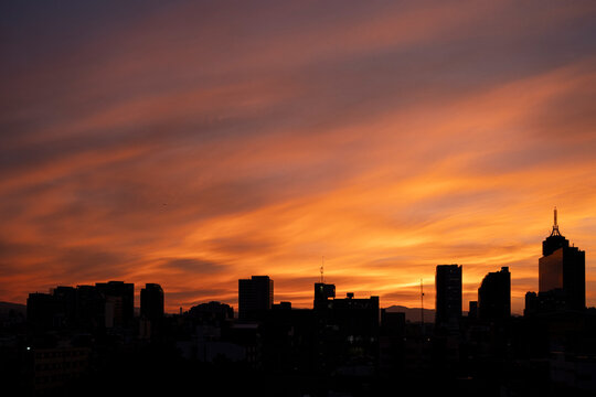 Silhouetted skyline at vivid sunset, Colonia del Valle, Mexico City, horizontal framing emphasizing urban profile and intense orange light in the sky