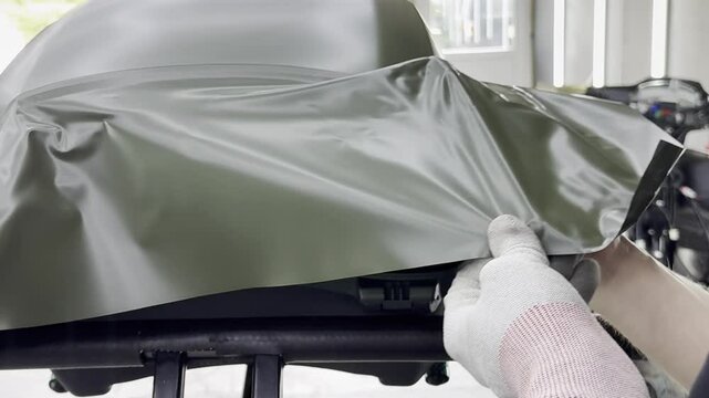 A specialist in wrapping a car with green khaki colored vinyl or ppf film in the process of work. Car wrapping specialists cover the car with green vinyl film. Khaki green vinyl foil. Selective focus.