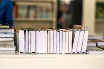 Stack of hardcover books lined up on white shelf in bookstore environment. Concept of books, reading habits, literature, publishing