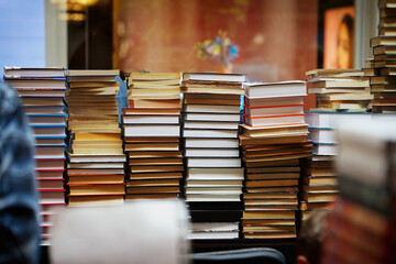 Tall piles of various books stacked together in indoor store setting. Tower of Knowledge, stacked wall of books. Concept of books, literature abundance, choice overload and printed knowledge
