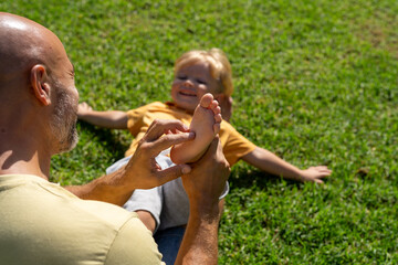 family and love concept - young father tickling his little son in park. close-up of a child's heel and the father's hand who tickles him. cheerful baby laughs from being tickled