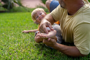 family and love concept - young father tickling his little son in park. close-up of a child's heel and the father's hand who tickles him. cheerful baby laughs from being tickled