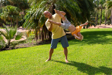 cheerful father holding baby upside down. father and son having fun on the green lawn in the park. funny family