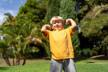 little strong boy portrait showing muscles . funny blond boy 4 years old shows muscles. baby in a bright T-shirt shows how strong he is. close-up portrait of a child