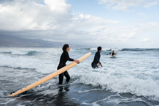 Surfers walking into ocean with surfboards, preparing to surf waves