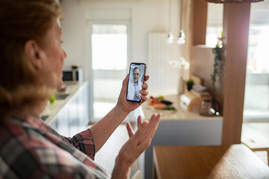 Senior woman having online video call with doctor at home using smartphone