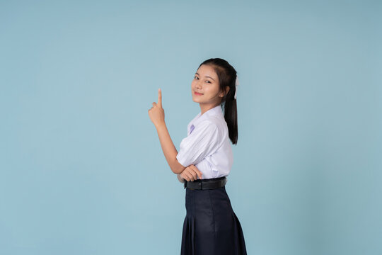 Looking into the camera, the high school girl is posing like a tutoring model on a blue background in studio, used for advertising materials that attract academic-minded teens.