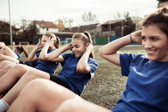 Teenage female soccer team performing sit ups during training on football field