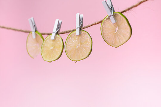 Limetten geschnitten an W&auml;scheklammern auf rosa Hintergrund Querformat