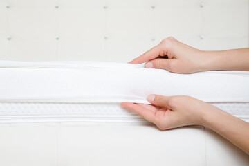 Young adult woman hands stretching and changing clean white bed sheet on mattress. Closeup. Front view.