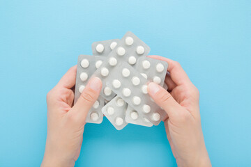 Young adult woman hands holding and showing blister packs with white pills on light blue table background. Pastel color. Closeup. Receiving vitamins or medication. Point of view shot. Top down view.