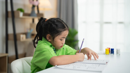 Young child engaged in creative study activity at home, focused on writing and learning in bright,...