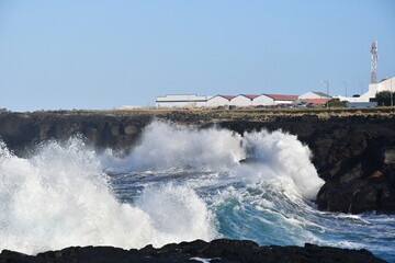 Dramatic Ocean Waves Crash Against Rocky Shoreline with Industrial background