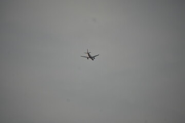 A solitary airplane soars across a vast, overcast sky.