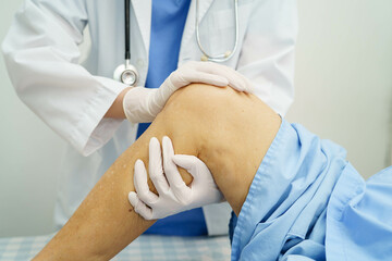 Doctor checking Asian elderly woman patient with scar knee replacement surgery in hospital.