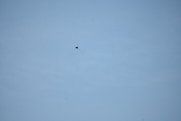 A tiny kite, a black speck, floats high in the clear blue sky.