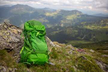 Adventure travel concept: bright green backpack on rocky peak overlooking scenic mountain landscape and rolling hills