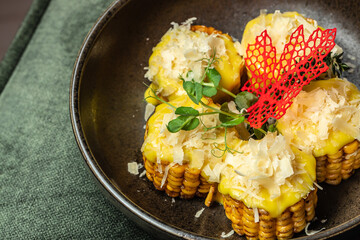 Grilled corn medallions topped with melted cheese, shaved parmesan, microgreens, and decorative garnish served in a dark ceramic bowl.