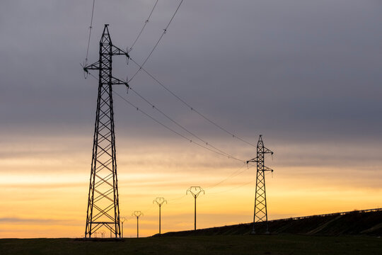 Electric transmission towers at dusk in Zaragoza, Spain, renewable energy grid infrastructure silhouetted against colorful sky in sustainable energy setting