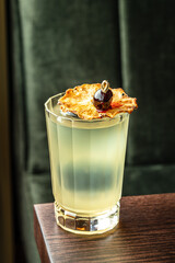 Tropical cocktail in a faceted glass topped with dried pineapple slice and dark cherry garnish on a wooden table with a dark velvet background