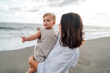 Mother holds child who points forward, suggesting future awareness, inspiration, toddler&rsquo;s gesture showing something beautiful. Happy and carefree childhood