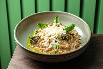 Creamy risotto garnished with shaved parmesan, basil leaves, and roasted vegetables served in a ceramic bowl on a dark wooden table