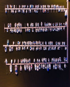 Overhead view of a modern marina with neatly lined boats in rows, docked in dark water. A symmetrical composition ideal for themes of organization and travel.