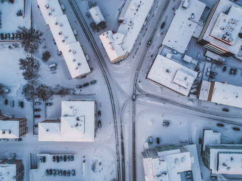 Snow-covered urban landscape viewed from above, showcasing rooftops, roads, and cars in a winter wonderland setting. A perfect blend of city life and seasonal charm.