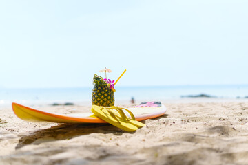 Beautiful decorated pineapple and flip-flops and surfboard left on the beach. Holidays, vacations,...