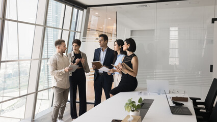 Five serious focused teammates gathered in skyscraper office meeting room for joint project...